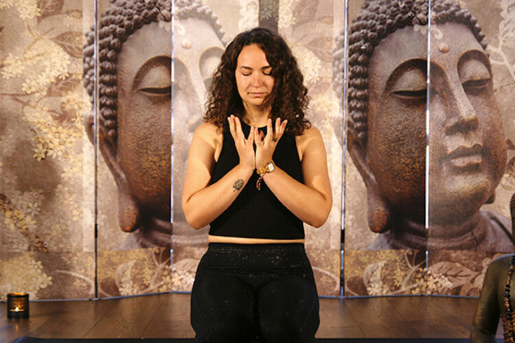 Frau kniet auf einer Matte während sie eine Meditation macht.