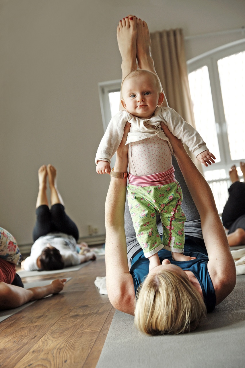 Frauen halten ihre Babys vor sich im Rückbildungsyoga im Yogaraum Ravensburg