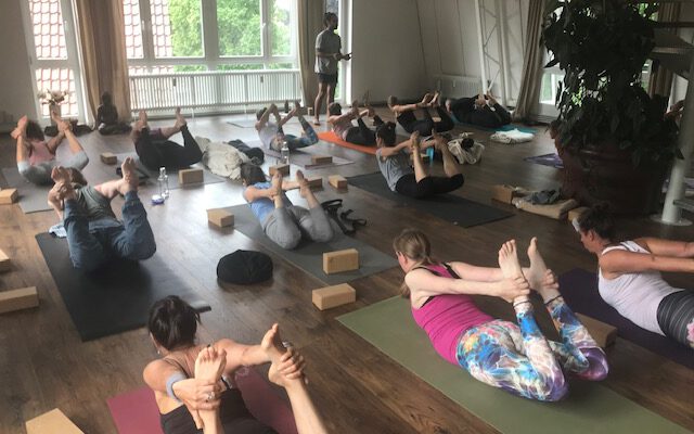 Die Gruppe des Yoga Workshops liegt in einer Yogaübung aum dem Bauch während sie den Anweisungen des Lehrers folgen.